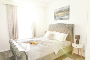 A neatly made bed with a grey headboard, a bedside table with a lamp, and a breakfast tray on the bed. - Victoria Road Apartment in Stoke (Stoke-on-Trent)