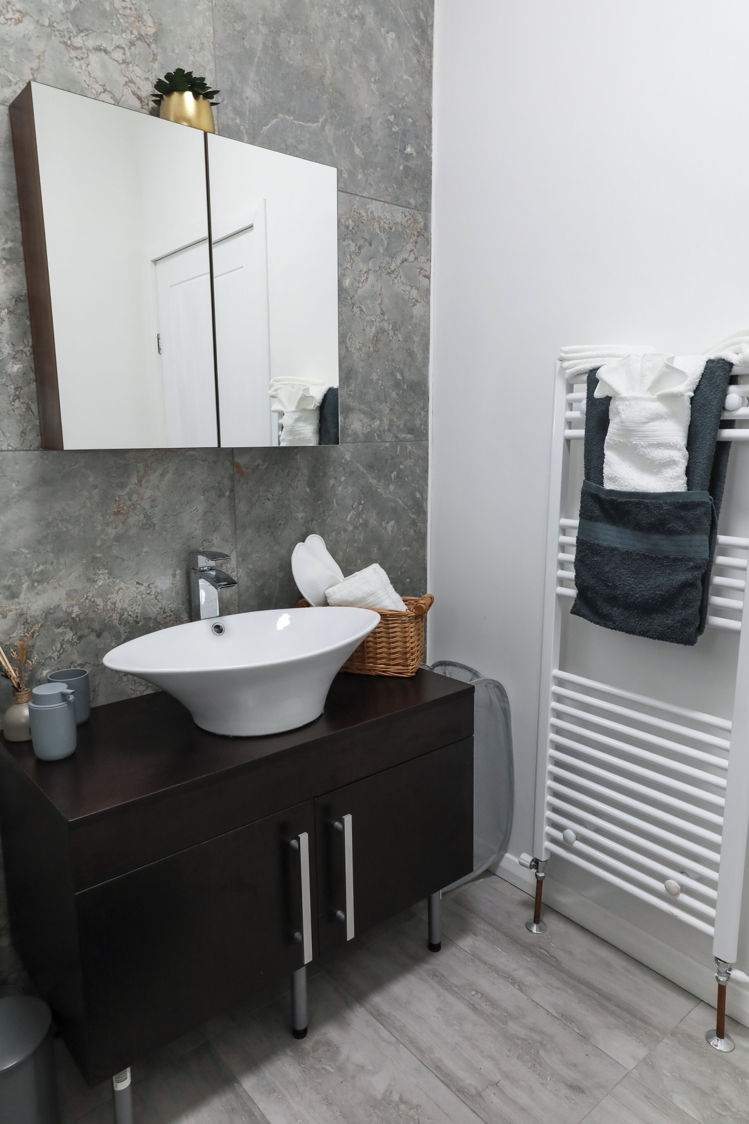 Un baño moderno con un tocador blanco, un espejo grande, un lavabo blanco y un perchero con toallas.