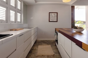 A modern kitchen with white cabinets, a wooden countertop, and a large window with blinds.