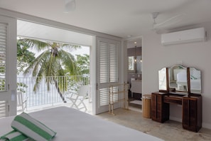 A bedroom with a large bed, a vanity with a mirror, and a view of palm trees through the balcony doors.