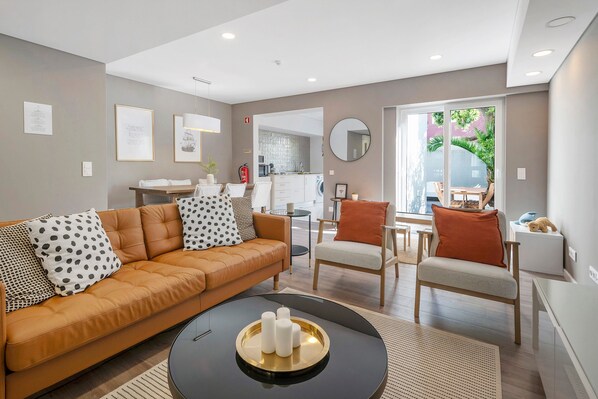 A modern living room with a sofa, chairs, a coffee table, and a kitchen in the background.