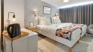 Een moderne hotelkamer met een bed, nachtkastjes, een waterkoker, een lamp en een groot raam met gordijnen.