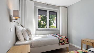 Una camera da letto con un letto, un comodino, una finestra con tende e una lampada a parete.