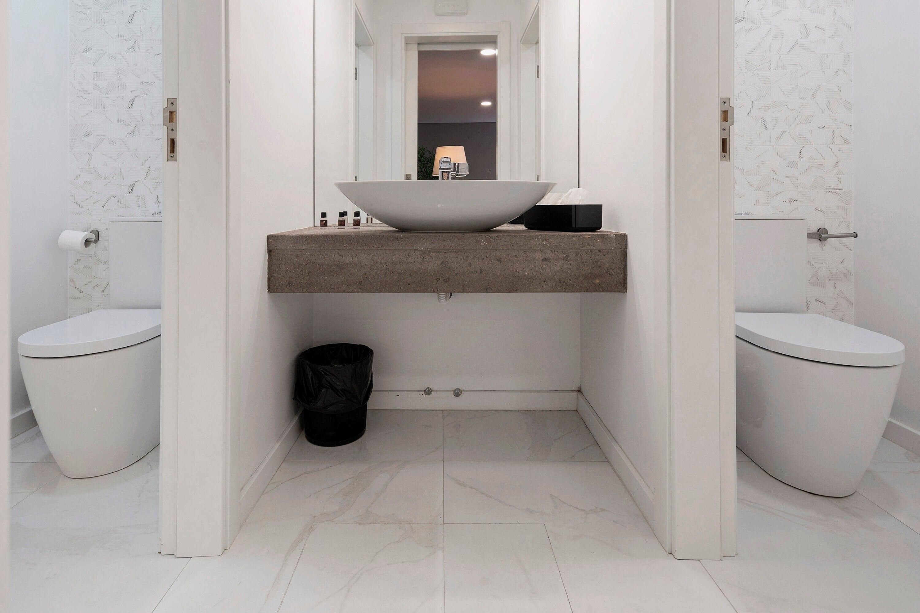 Ein modernes Badezimmer mit einem großzügigen Waschtisch, zwei Toiletten und einem Mülleimer.