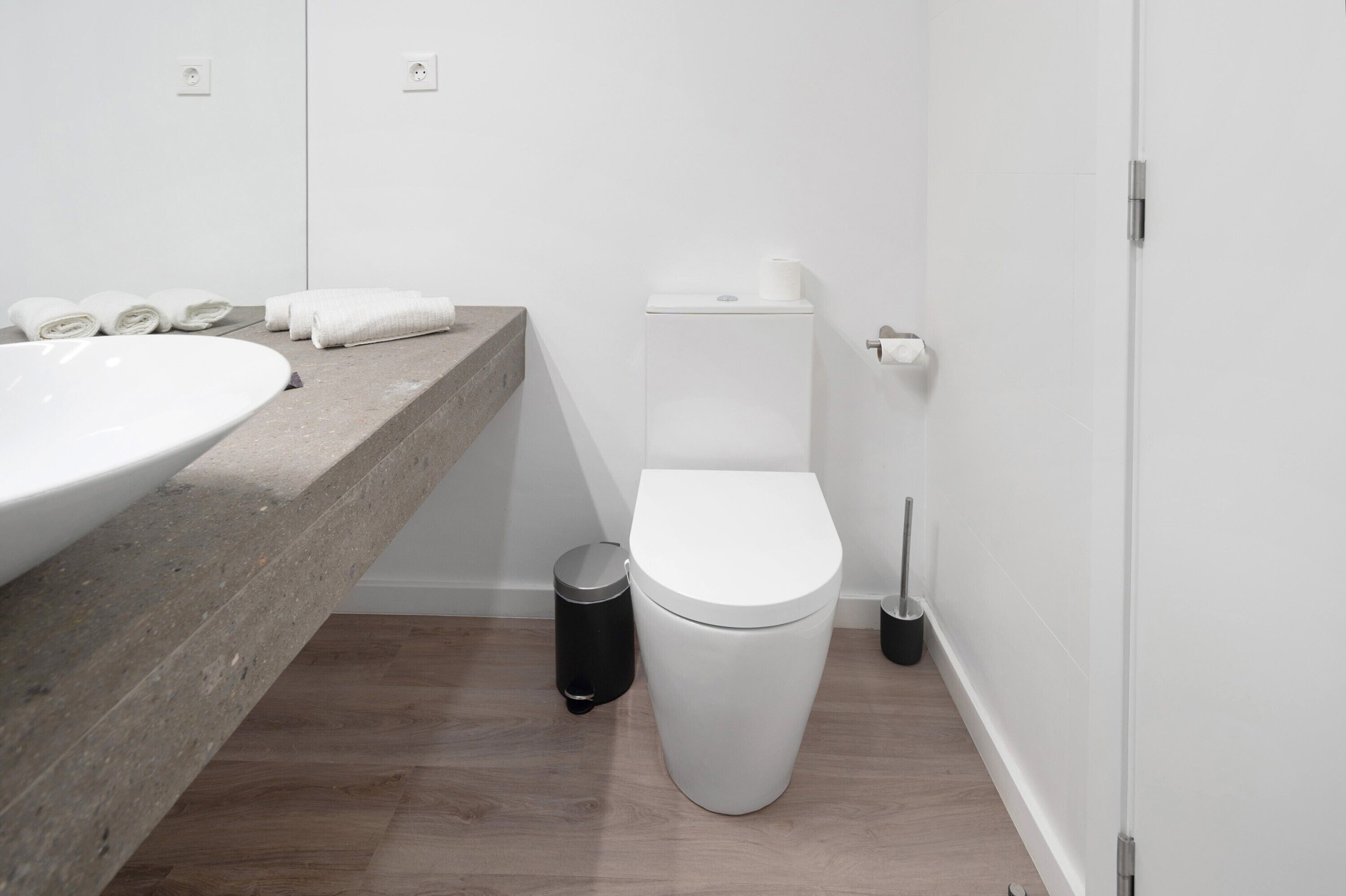 A modern bathroom with a large sink, toilet, and a trash bin.