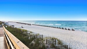 A beach with a wooden boardwalk, a row of beach chairs, and a wooden pier extending into the water. - NEW 2 Blocks to Camp WaterColor with LSV, Bikes, and more! (Santa Rosa Beach)