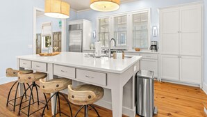 A modern kitchen with a central island, bar stools, a stainless steel sink, and a trash can. - NEW 2 Blocks to Camp WaterColor with LSV, Bikes, and more! (Santa Rosa Beach)