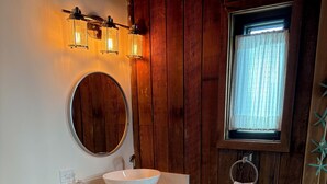 A bathroom with a white toilet, a round mirror, a white sink with a white towel, and wooden paneling on the walls.