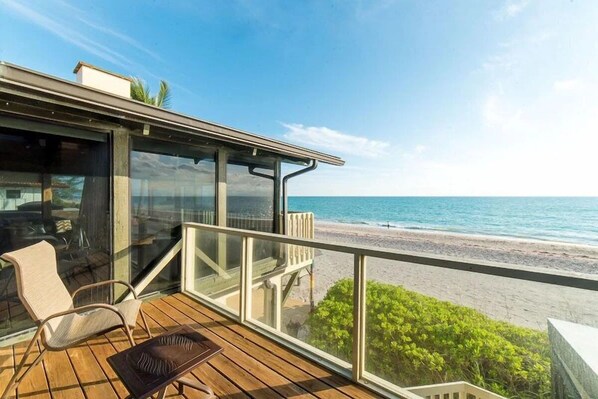Une terrasse en bois dotée d’une balustrade en verre, qui offre une vue sur la plage.