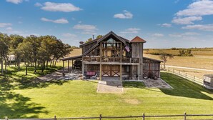 A rustic wooden building with a balcony, surrounded by a fenced property and trees. - The Barn at Quail Creek Ranch - 2 Bedroom Peaceful Ranch Retreat (Wheeler)