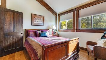 A bedroom with a wooden bed, a nightstand, a lamp, and a window with blinds.