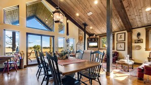 A spacious dining area with a high ceiling and large windows, wooden flooring, and a central table with chairs. - The Barn at Quail Creek Ranch - 2 Bedroom Peaceful Ranch Retreat (Wheeler)