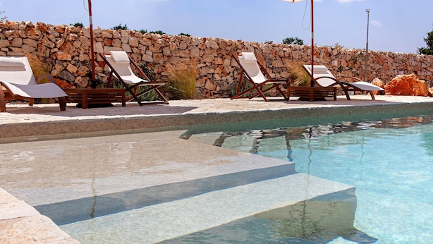 Ein Poolbereich mit Liegestühlen und einer Steinmauer.