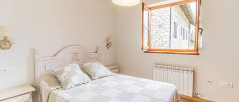 Quarto com cama, mesa de cabeceira, luminária, janela e radiador.