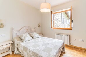 A bedroom with a bed, a nightstand, a lamp, a window, and a radiator. - Charming Pyrenean Flat with Terrace, Views & Pool (Anciles)