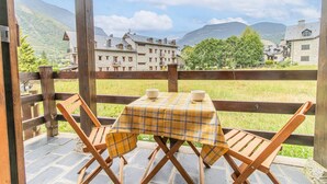 Una terraza de madera con una mesa y sillas, con vistas a un paisaje montañoso con edificios tradicionales.