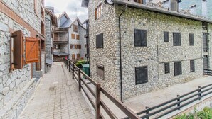 Un estrecho sendero de piedra flanqueado por edificios de piedra tradicionales con contraventanas y balcones de madera, que conduce a una escalera de madera.
