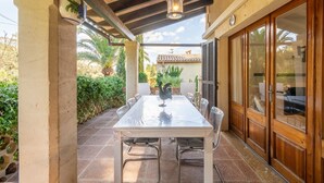 A covered patio with a table and chairs, a decorative rooster, and a view of a house with a tiled roof. - Authentic Mediterranean Villa (Cala Sant Vicenç)