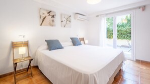 A bedroom with a bed, a chair with a lamp, and a view of greenery through a sliding door. - Authentic Mediterranean Villa (Cala Sant Vicenç)
