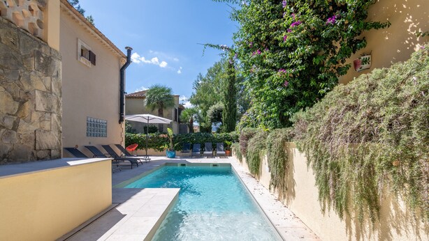 A swimming pool with lounge chairs, a stone wall, and a building with a window. - Authentic Mediterranean Villa (Cala Sant Vicenç)