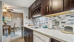 A modern kitchen with dark wood cabinets, a white dishwasher, and a tiled backsplash. - Amelia Island 2BR Beach Getaway (Fernandina Beach)