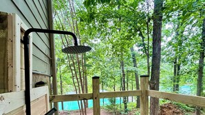 A wooden deck with a showerhead, a wooden fence, and a view of a forest.