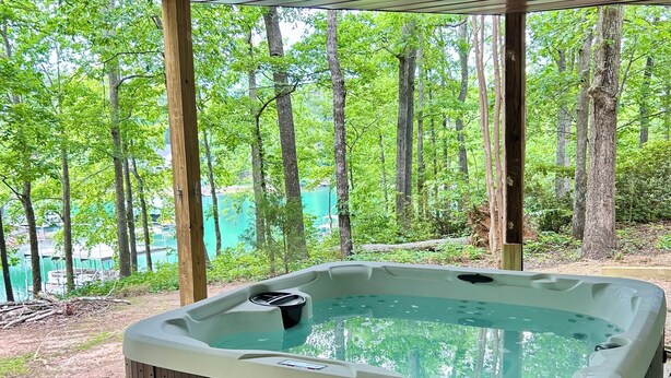 A hot tub under a wooden deck with a view of a forested area.