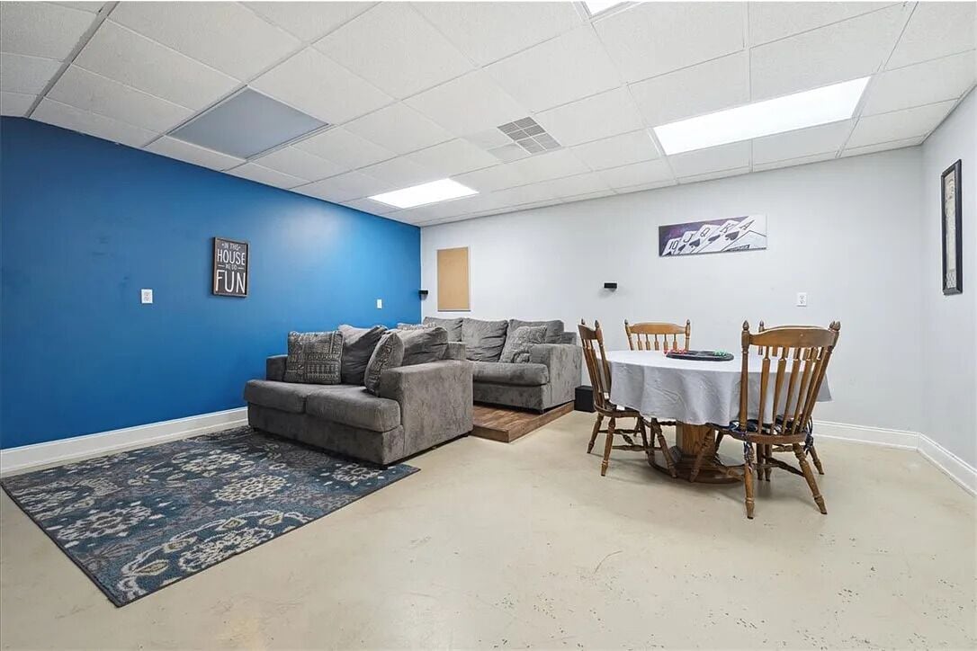 Une pièce avec un mur d’accent bleu, un canapé gris, une table à manger avec des chaises et un tapis.