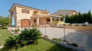 Una casa de dos pisos con un porche cubierto, piscina y un jardín bien cuidado.