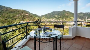 A balcony with a glass table, chairs, a teapot, and a book. - Traveller's House Holiday Home with Mountain View, Shared Pool, and Wi-Fi (Madeira Machico)