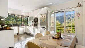 A modern kitchen with a dining area, large windows, and a view of the outdoors. - Traveller's House Holiday Home with Mountain View, Shared Pool, and Wi-Fi (Madeira Machico)