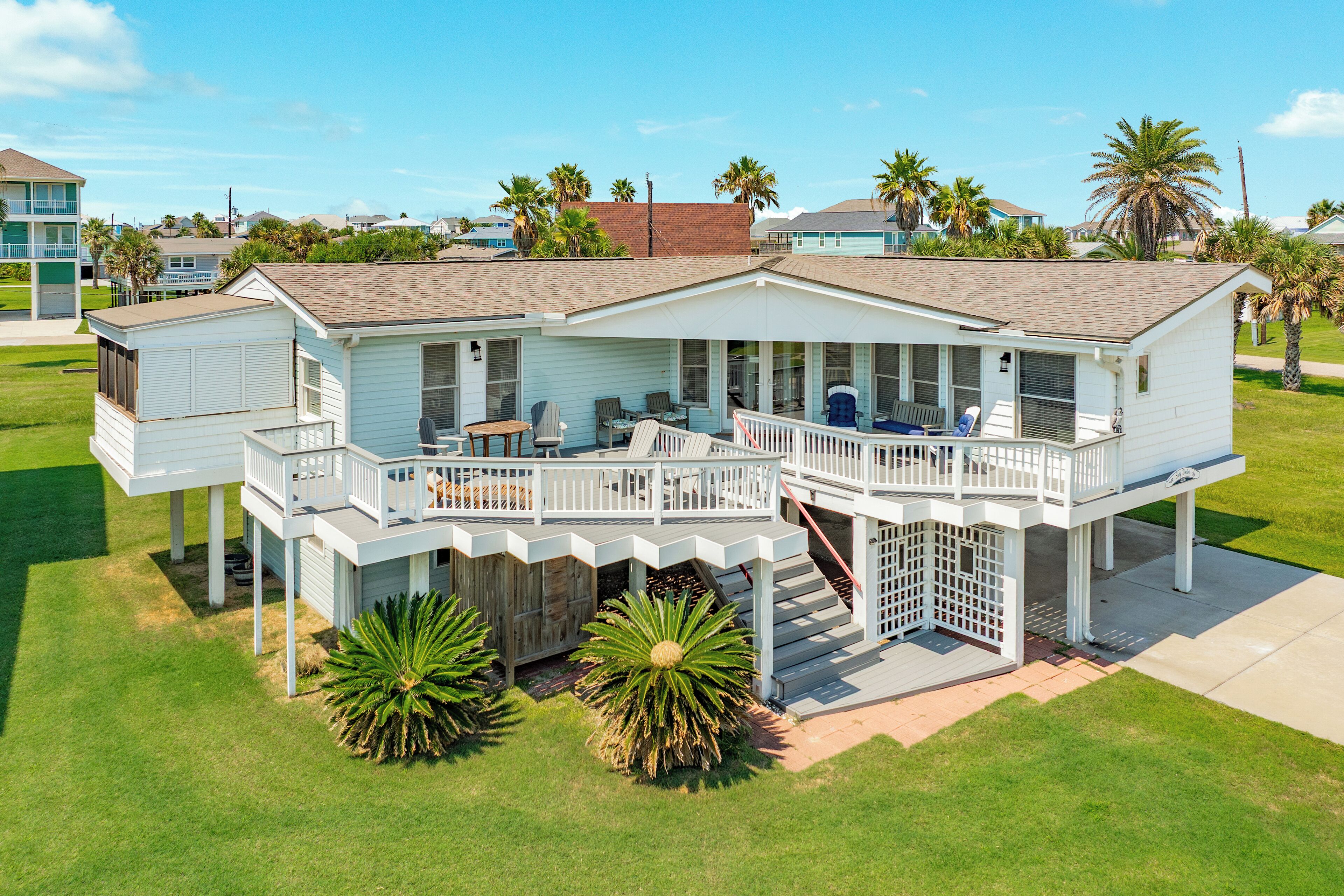 A two-story house with a balcony and a covered porch, surrounded by a well-maintained lawn and palm trees.