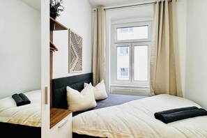 A bedroom with a bed, a bedside table, a mirror, and a window with curtains.
