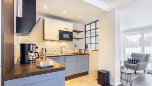 A modern kitchen with a microwave, coffee maker, and kettle. There is a window with blinds and a grey armchair. - Apartment 'Jost' with Private Terrace, Shared Garden, and Wi-Fi (Sundern)