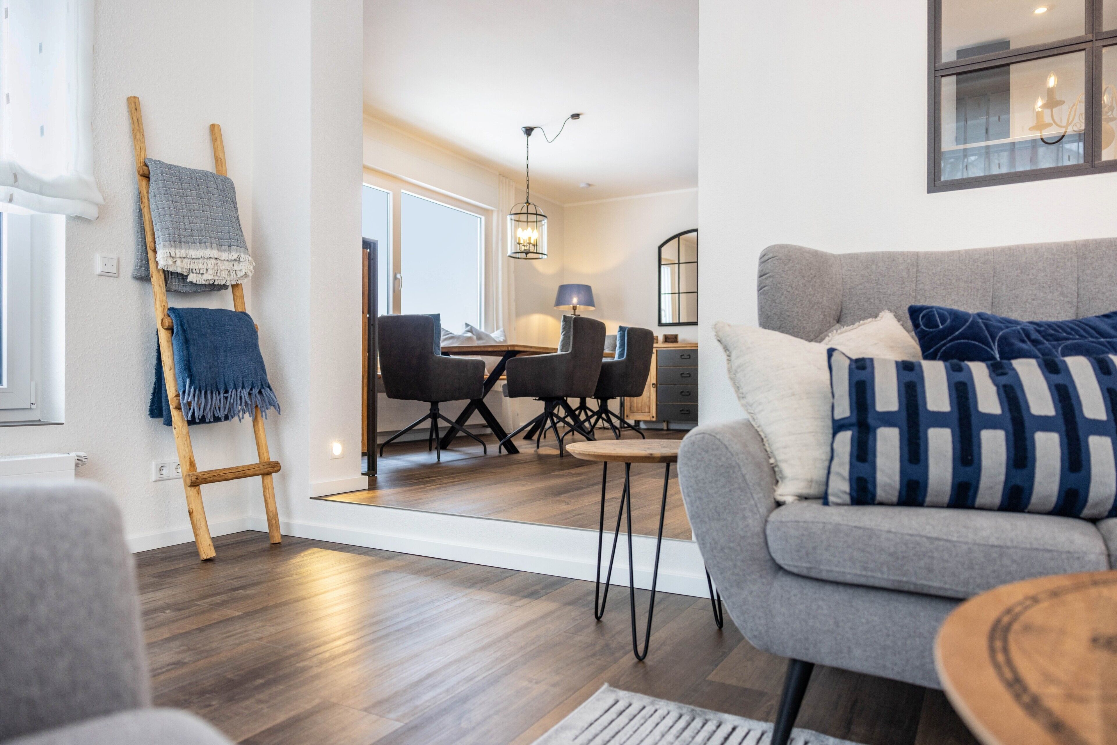A modern living room with a grey sofa, wooden floor, and a dining area with black chairs and a table.