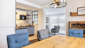 A modern kitchen with white cabinets, a microwave, and a sink. There is a dining area with a wooden table and blue upholstered chairs. - Apartment 'Jost' with Private Terrace, Shared Garden, and Wi-Fi (Sundern)