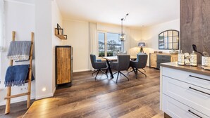 A modern kitchen with wooden flooring, a dining area with chairs, a wooden cabinet, and a large window with a view. - Apartment 'Jost' with Private Terrace, Shared Garden, and Wi-Fi (Sundern)