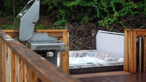 Ein Whirlpool auf einer Holzterrasse mit Holzwand, umgeben von viel Grün.