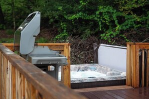 A hot tub on a wooden deck with a wooden railing, surrounded by greenery.