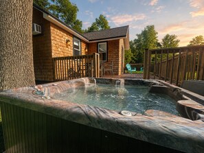 Un bain à remous avec une terrasse en bois, une maison en briques et un arbre en arrière-plan.