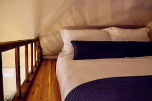 Ein Bett mit weißer und dunkelblauer Bettwäsche, ein Holzboden und eine Holzreling.