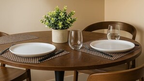 Ein runder Esstisch mit zwei weißen Tellern, Besteck und einem klaren Glas. In der Mitte steht ein Blumentopf.
