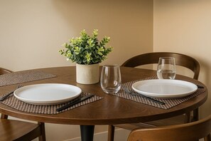 A round dining table with two white plates, cutlery, and a clear glass. A potted plant is placed in the center.