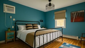 Ein Schlafzimmer mit Bett, Nachttischen, einem Fenster mit Jalousien, einem Heizkörper und einem Deckenventilator.