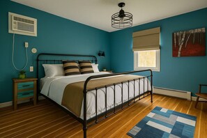A bedroom with a bed, bedside tables, a window with blinds, a radiator, and a ceiling fan.