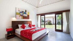 A spacious bedroom with a large bed, a ceiling fan, and a sliding glass door leading to a garden.