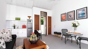 A modern living room with a sofa, coffee table, and a dining area with chairs and a table. There is a kitchen area with a refrigerator, microwave, and a cabinet. The room has white walls and a ceiling fan. - Lovely Pool Villa | Short Walk to Potato Head Club (Kerobokan Kelod)