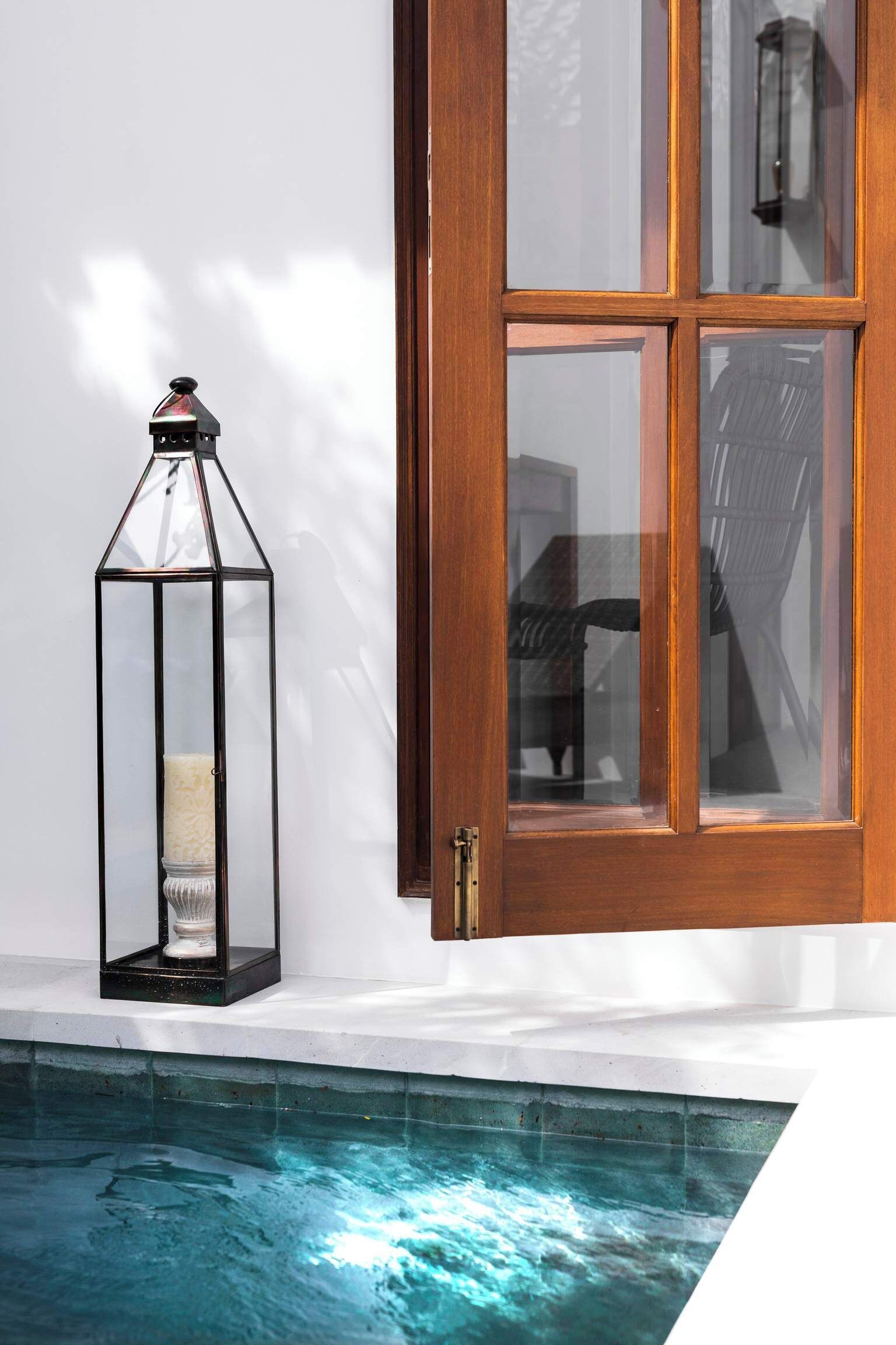 Un espace aménagé au bord de la piscine, avec une lanterne en verre et une porte en bois.