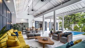 A spacious living area with a pool, yellow and green sofas, wooden coffee table, and a dining area with chairs and a table.