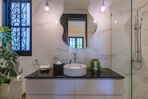 Un baño moderno con un lavamanos redondo, un espejo grande y una ducha.